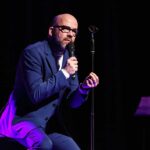 Lutz von Rosenberg-Lipinsky live auf der Bühne - sitzend mit Mikrofon in der Hand
